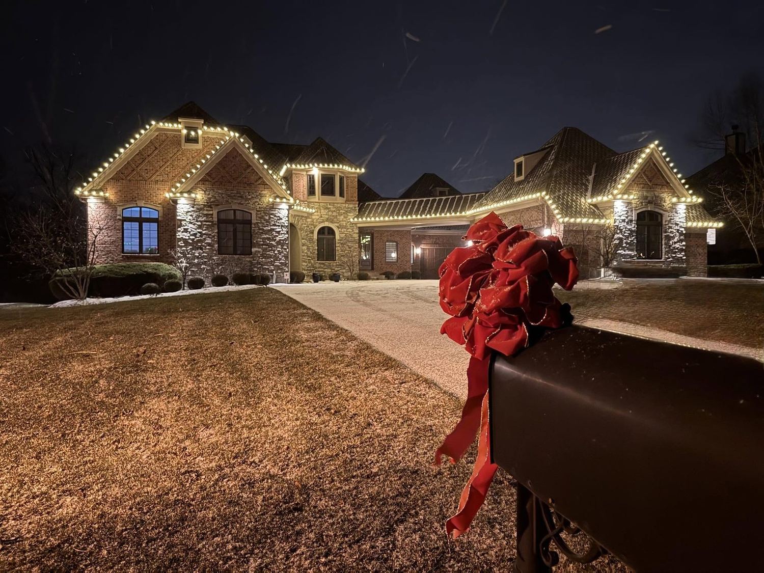 A red bow at the driveway with the house glowing behind it, a Mike’s Cincinnati Christmas Lights install